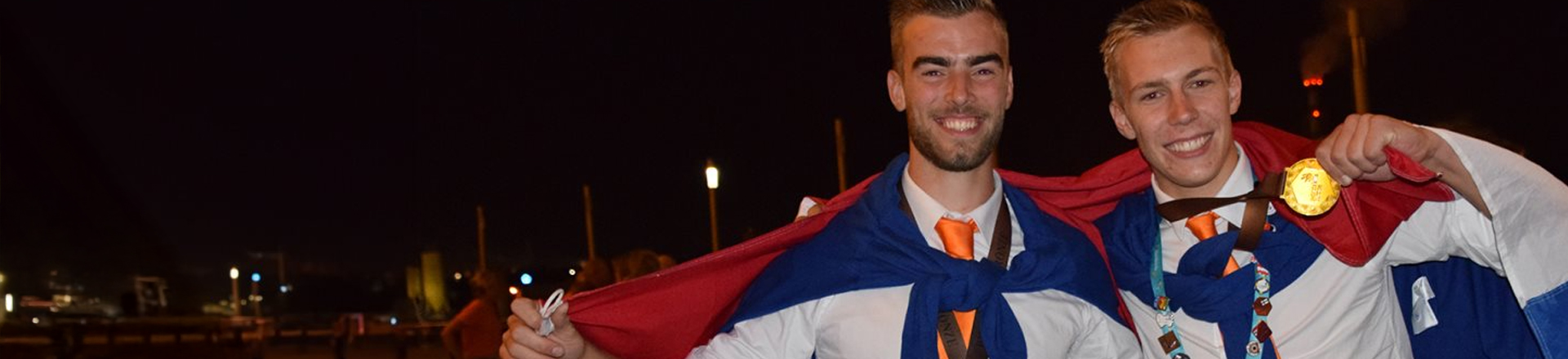 Twee blije studenten met nederlandse vlag en medaille.