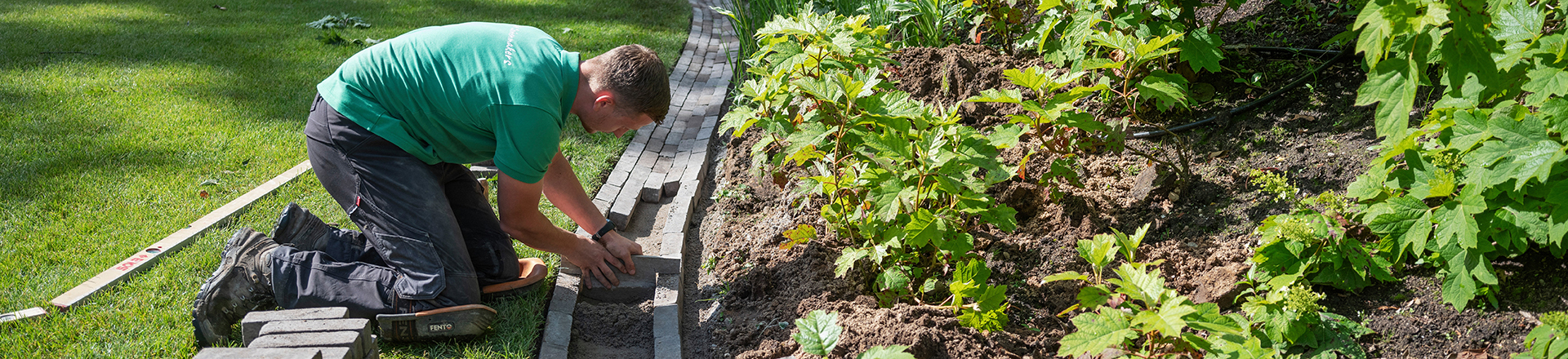 Student hovenier en groenvoorziening legt tegels in een groene tuin.