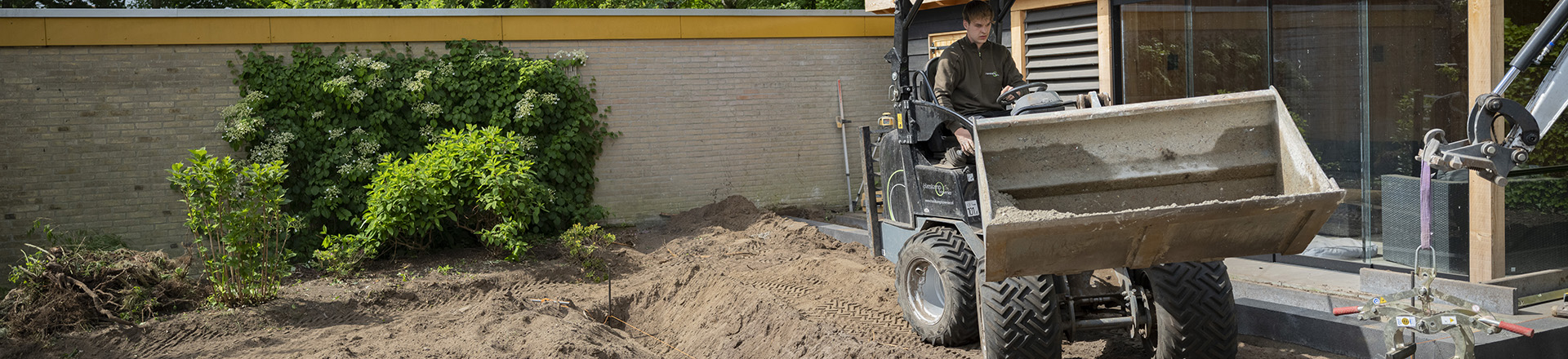 student hovenier en groenvoorzieining bezig met kleine shovel in een tuin in aanleg.
